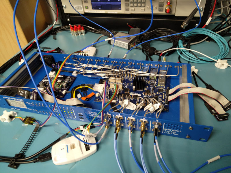 Blue 1U case with the logic board inside, cables coming off of many connectors on the PCB, and many aluminum semi-rigid cables coming off to front/rear panel ports