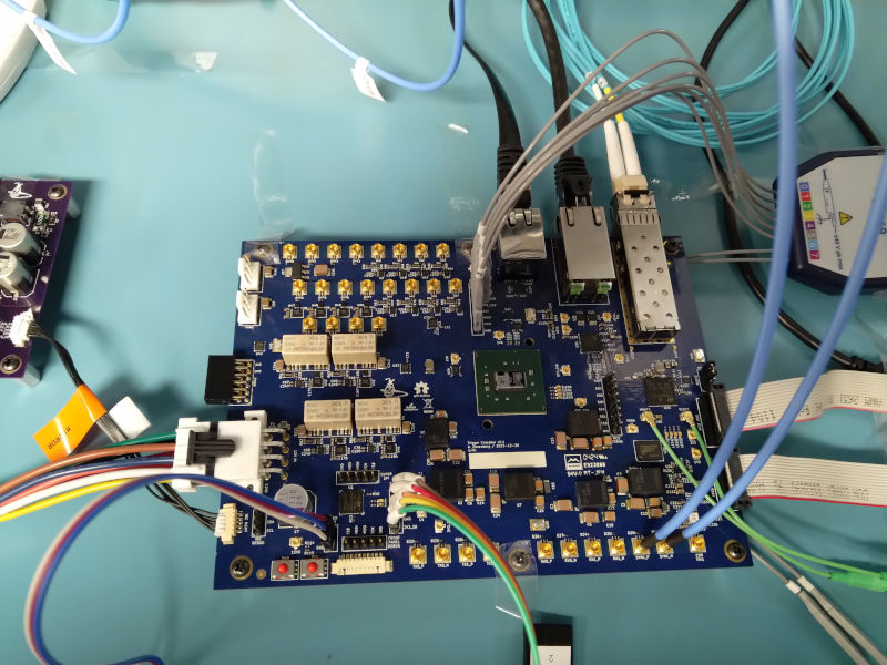 Photo of a blue PCB covered in SMPM connectors with probe cables connected to various headers and test points