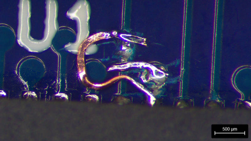 Blue PCB with a QFN seen under a microscope with two tracks cut and swapped with bare copper jumper wires