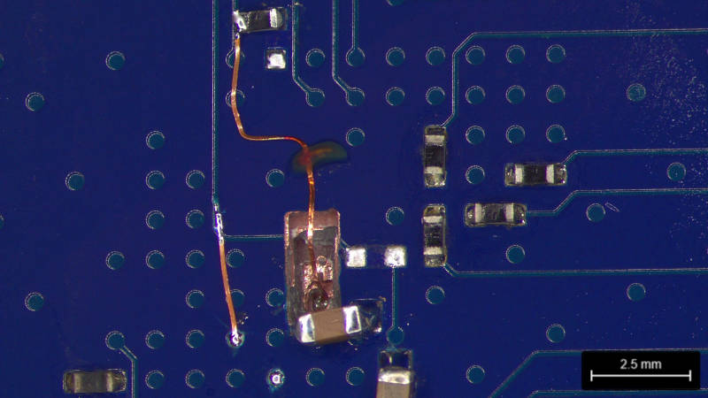 Microscope view of finished rework with wire coming out of the hole and connected to a surface track