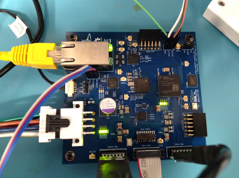 Photo of test board with RJ45 jack and Ethernet PHY in the top left corner, Spartan-7 FPGA right center, MCU in the middle, and power inlet in the bottom left