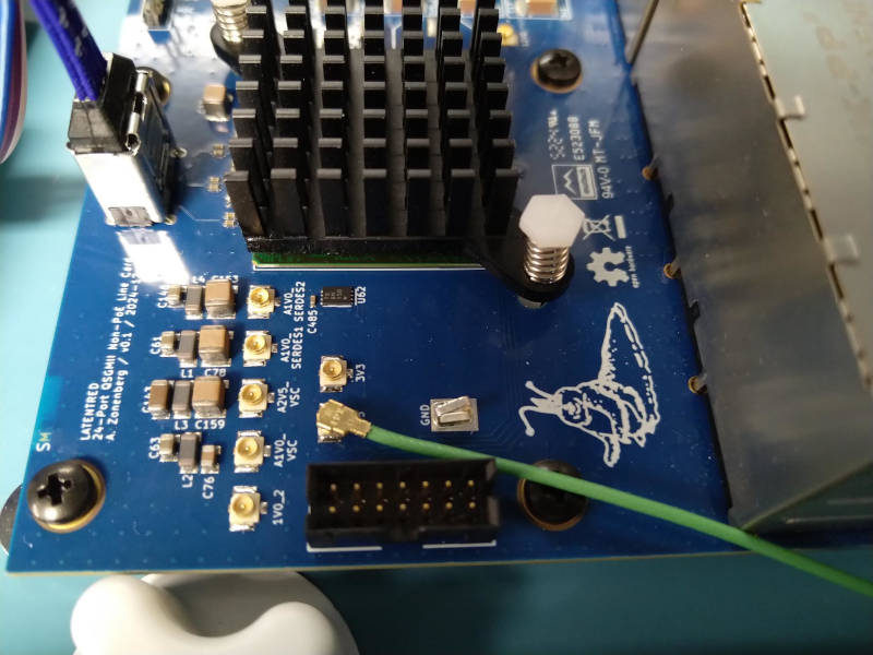 Blue PCB with a large IC under a heatsink at the top and a row of U.FL connectors below it, with a green coaxial cable coming off one