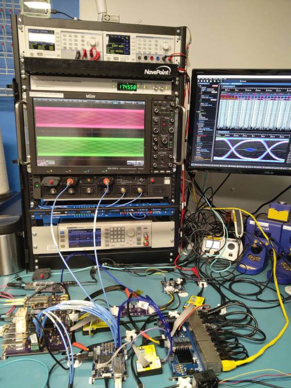 Entire lab setup showing the line card, FPGA board, adapters and cables, and two blue coaxial cables going up to an oscilloscope on a rack
