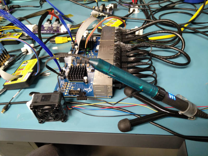 Line card on a lab bench surrounded by cables with a blue-green differential probe on a stand connected to a solder-in tip on the board